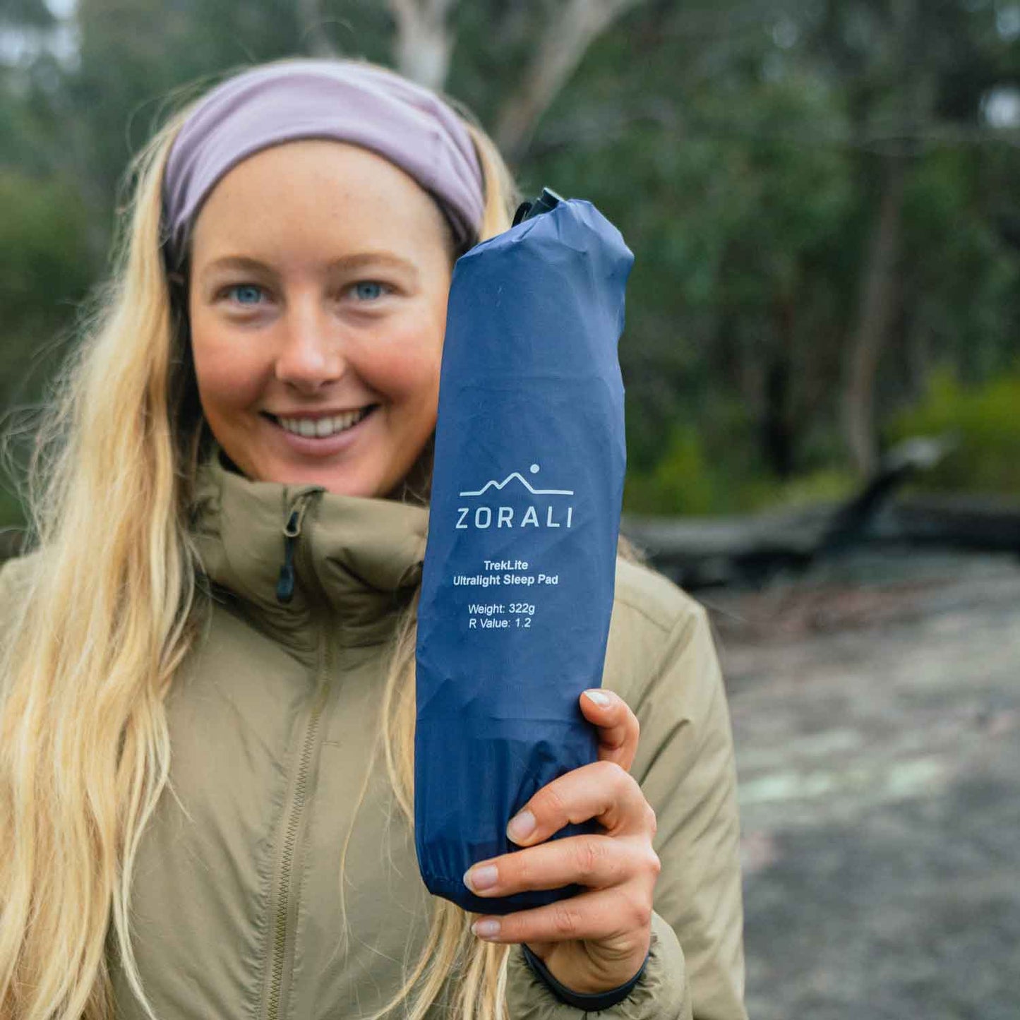 Person holding a ZORALI sleeping pad in a forest setting