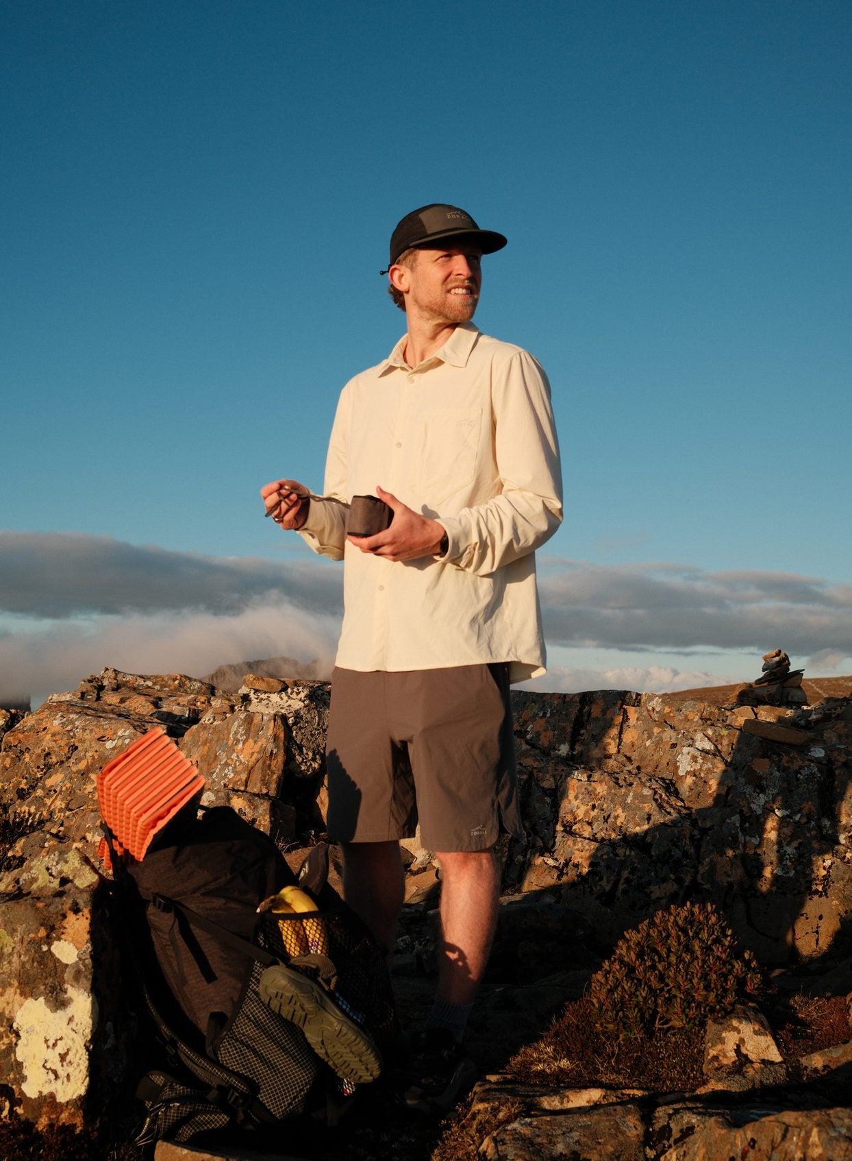 Cam at a summit stop under a blue sky in the Beachwood Daylight™ Technical Long Sleeve Shirt