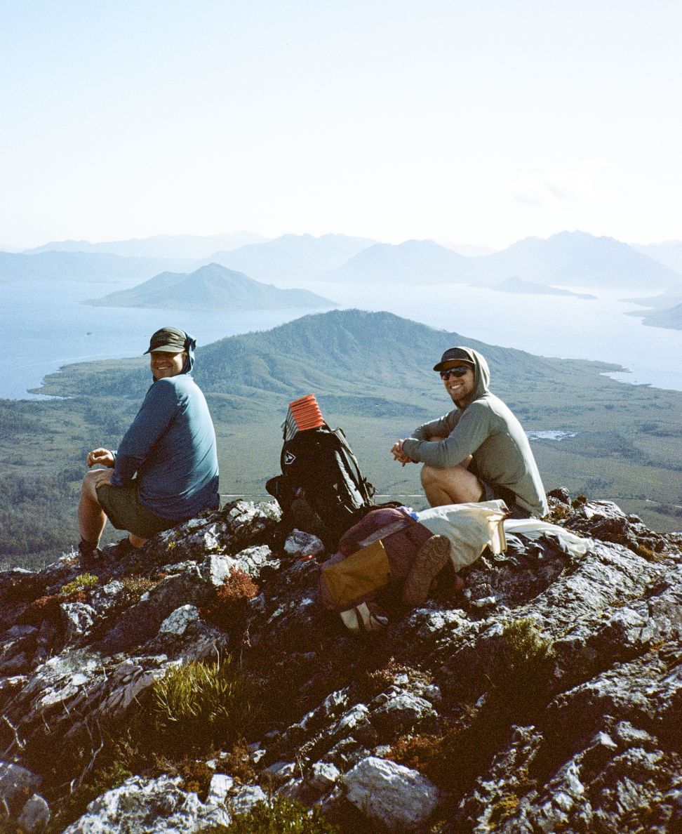 Two hikers sitting on a summit with their packs, above a lake