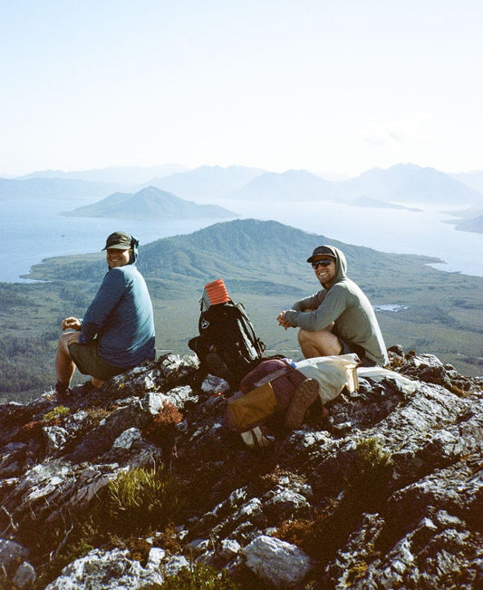 Two hikers sitting on a summit with their packs, above a lake