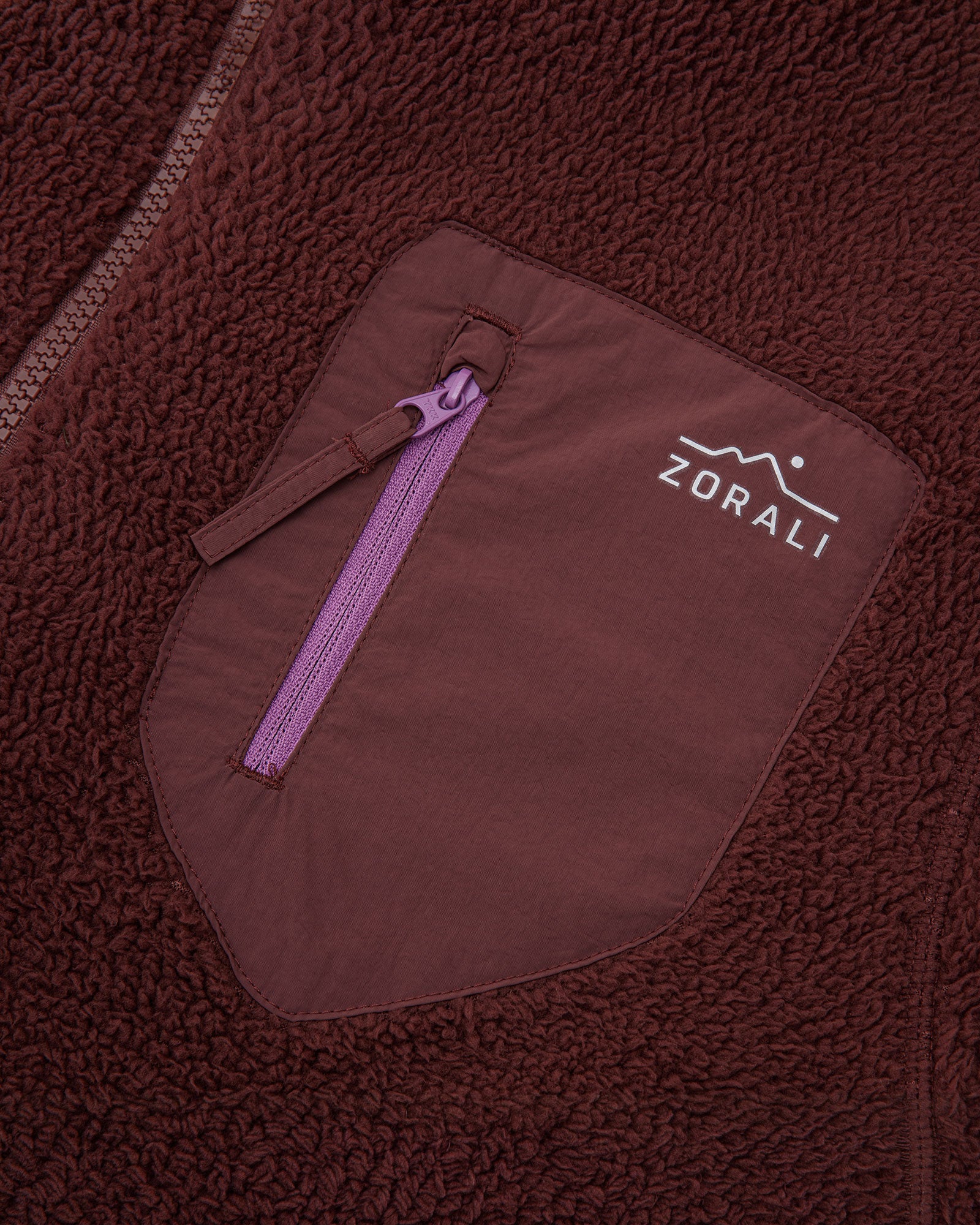 Close-up of the maroon chest pocket with purple zipper pull and Zorali logo on the Cosy Camp fleece jacket.