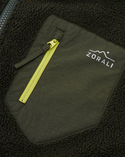 Close-up of the olive green chest pocket with yellow zipper pull and white Zorali mountain logo on a dark green sherpa fleece jacket.