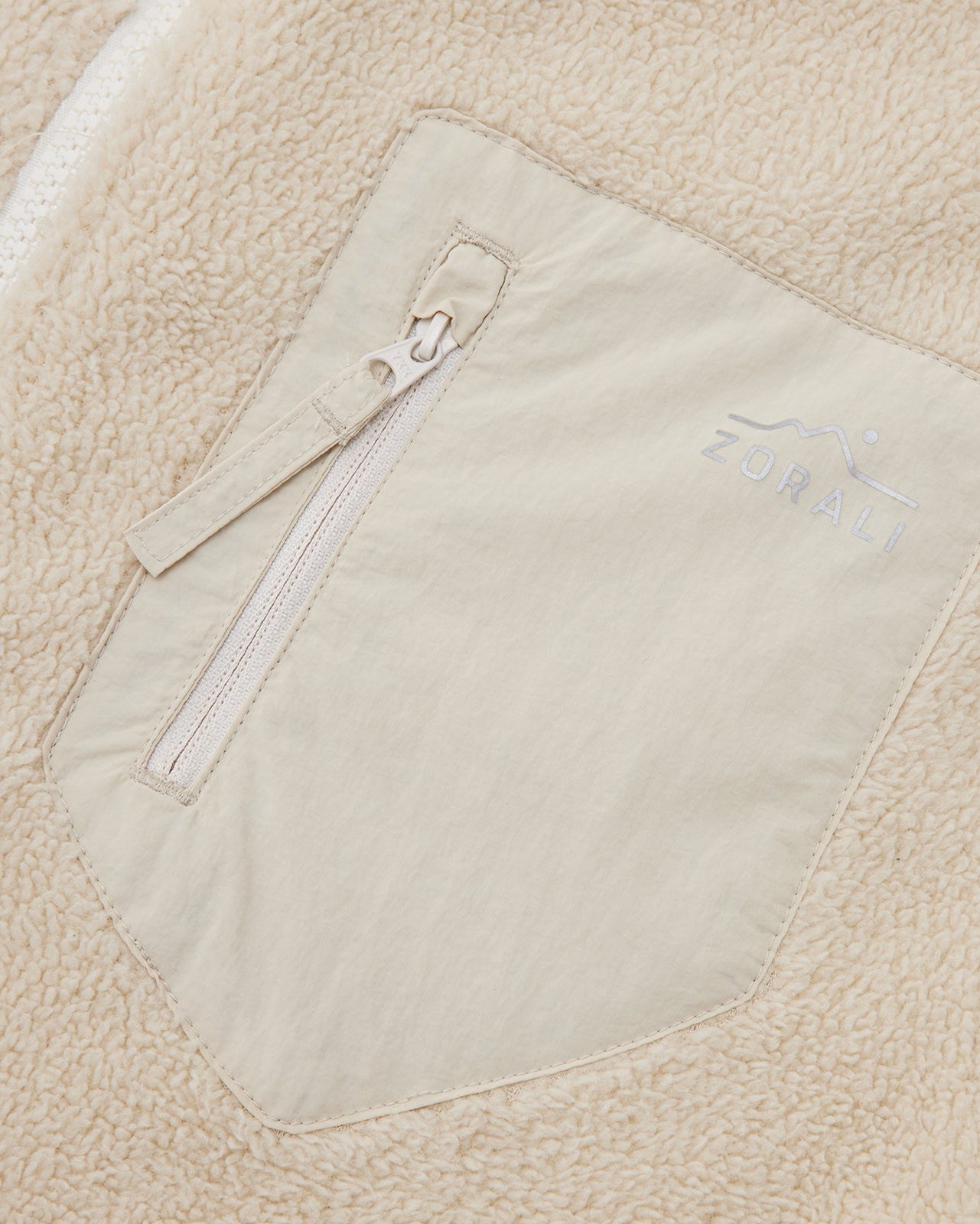 Close-up of the cream chest pocket detail on a Cosy Camp fleece jacket, showing the Zorali logo.