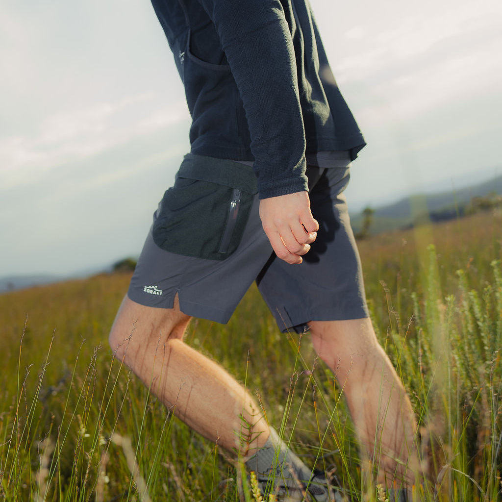Person walking through tall grass wearing a dark long-sleeve shirt and shorts.