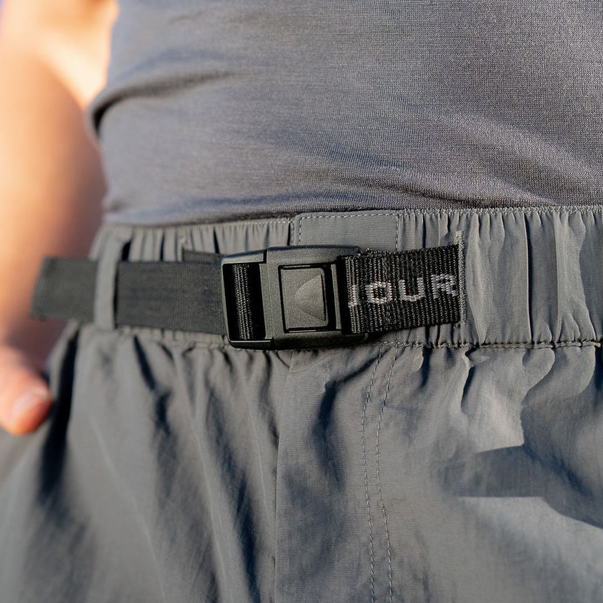 Person wearing a gray sleeveless shirt and pants with a black belt featuring 'OUR' branding.