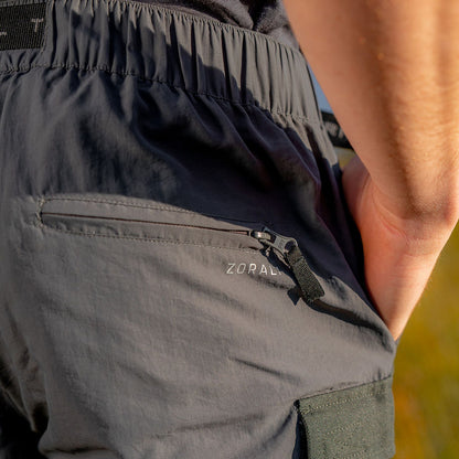 Person wearing dark gray pants with zippers in a natural setting