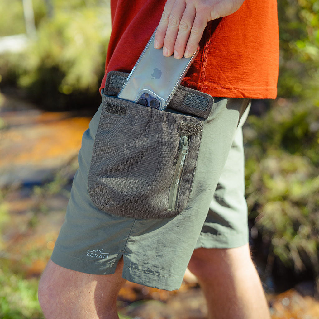 Person wearing a red shirt and green shorts with a phone in a pocket, outdoors.
