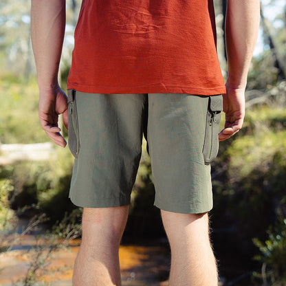 Person wearing a red shirt and green shorts standing outdoors with a blurred natural background