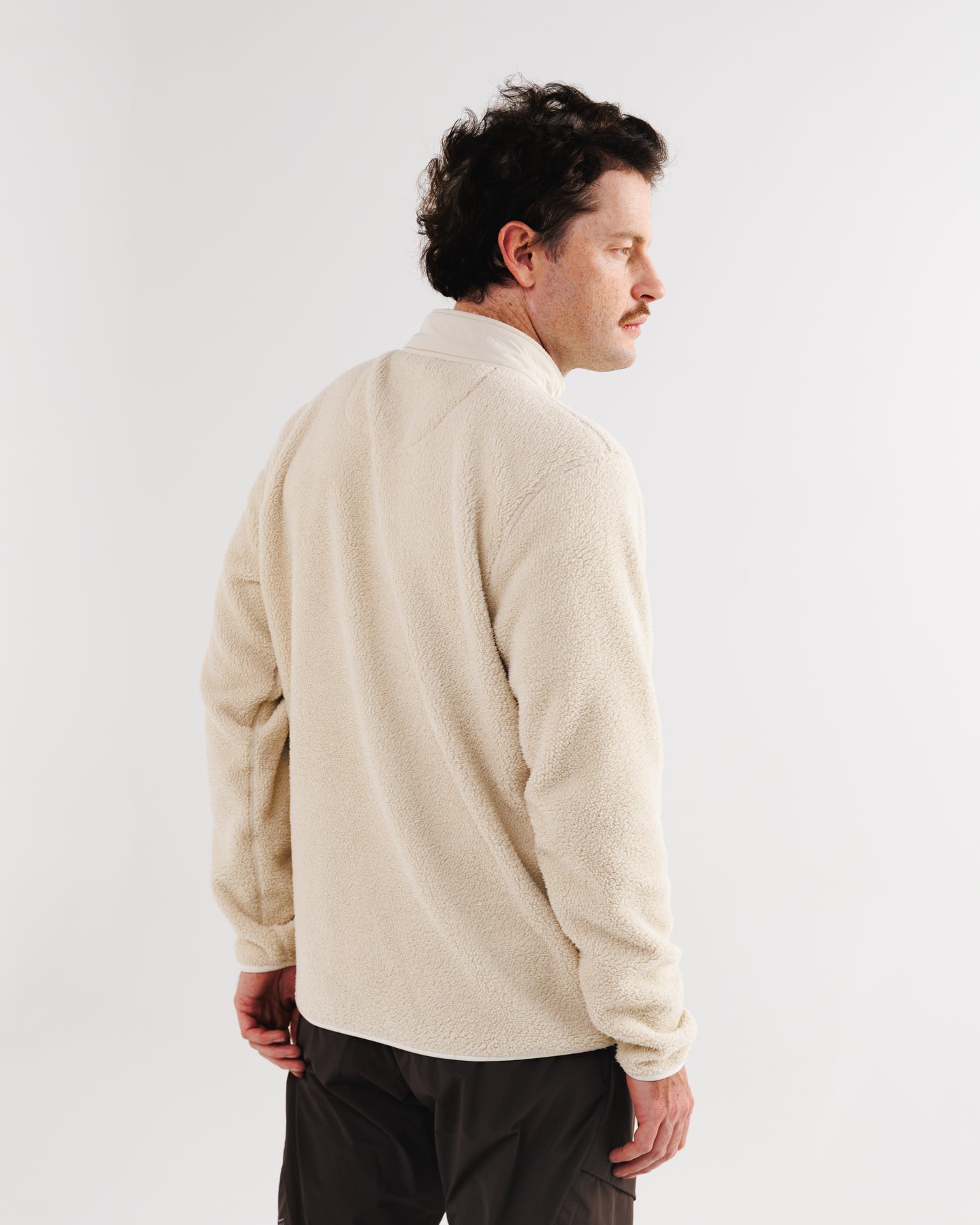 Back view of a man wearing a cream sherpa fleece jacket with the collar turned up.