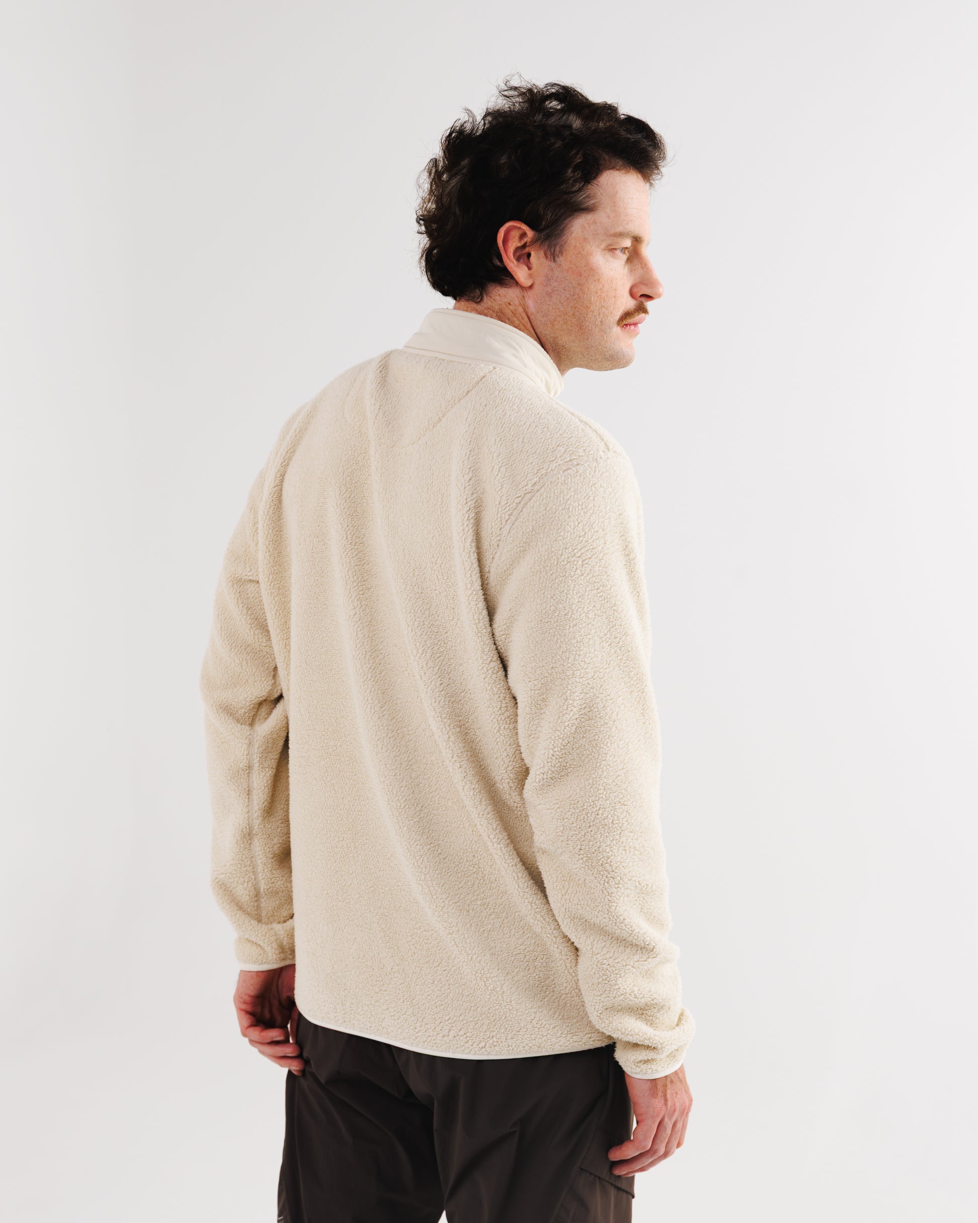 Back view of a man wearing a cream sherpa fleece jacket with the collar turned up.