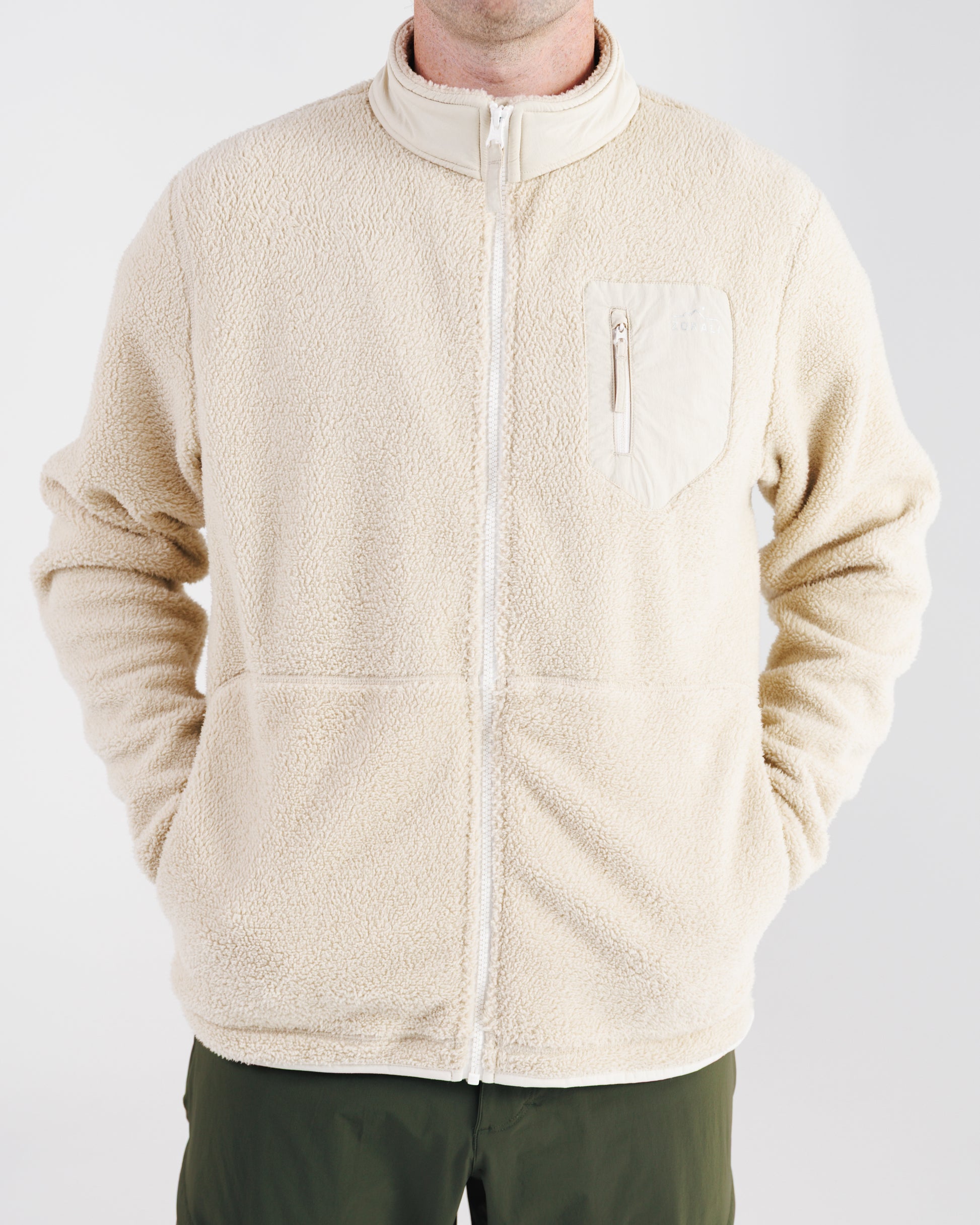 Man wearing a cream sherpa fleece zip-up jacket, front view with hands in pockets.