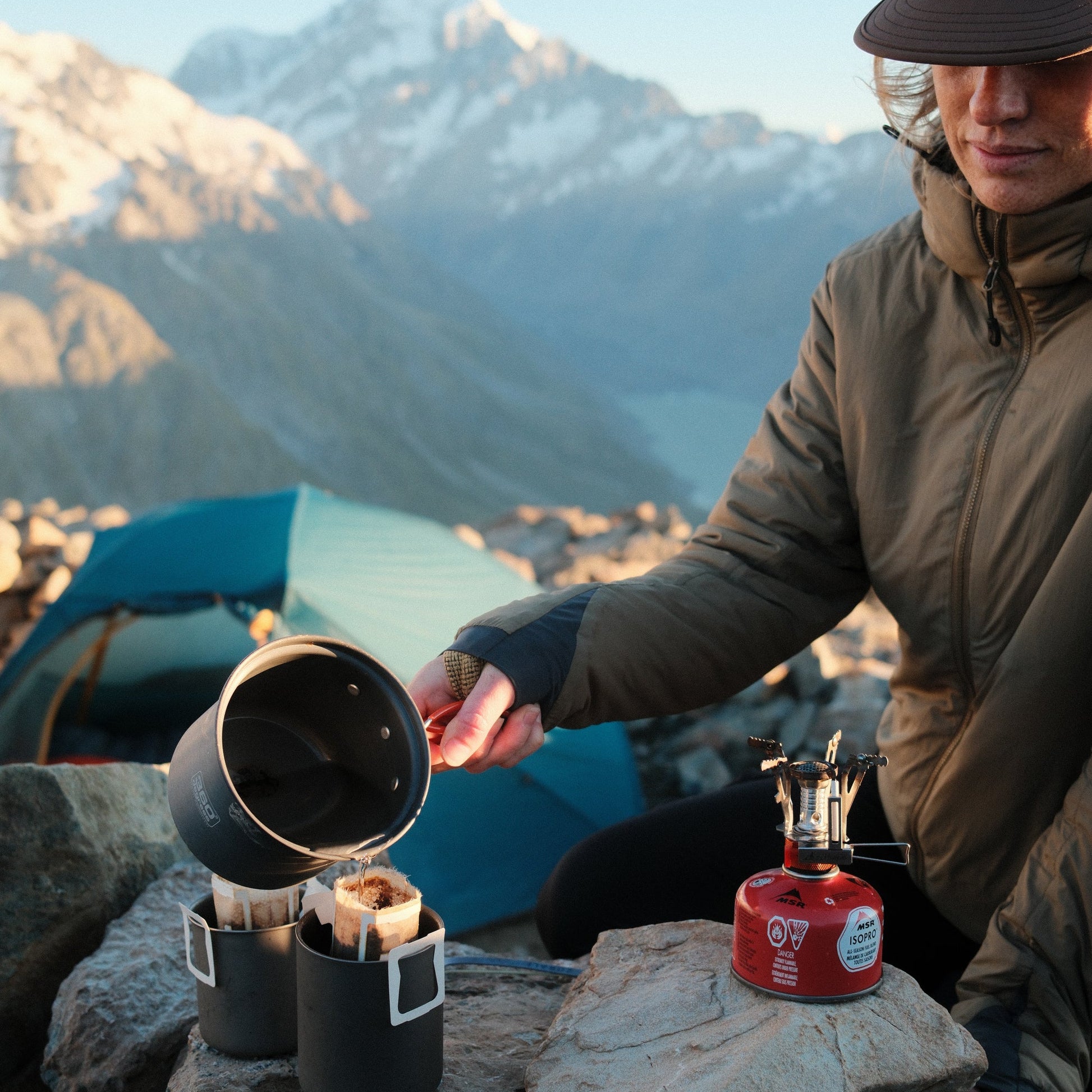 Person preparing a camping stove with a scenic mountain backdrop