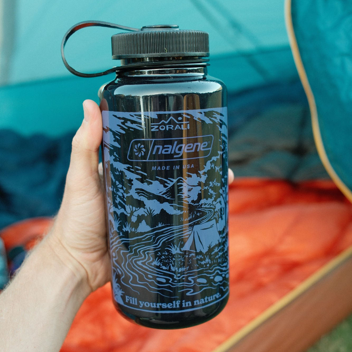 Nalgene water bottle with nature-themed design held by a person in front of a tent.