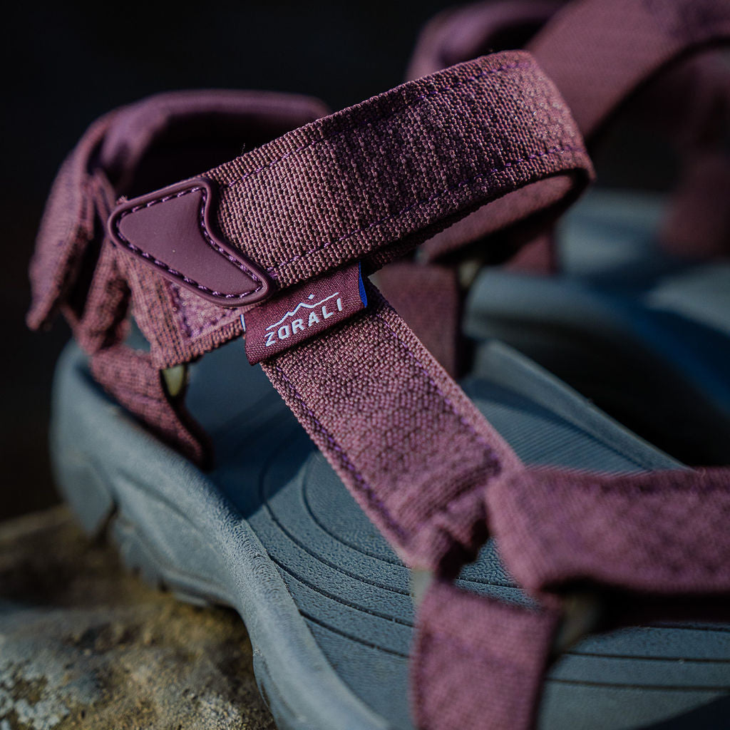 Close-up of a sandal with purple straps and 'Zorali' branding on a dark background