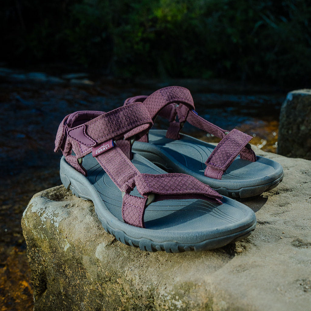 Pair of purple and gray sandals on a rock with a natural background