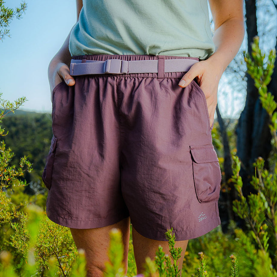 Person wearing purple shorts standing in a natural setting with trees and flowers.