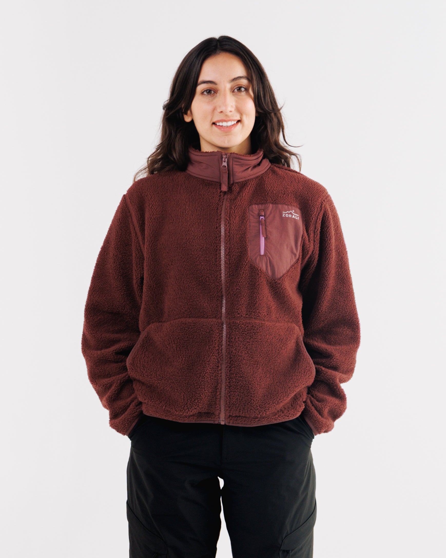 Woman wearing a maroon Cosy Camp fleece zip-up jacket, front view with black pants, smiling at camera.