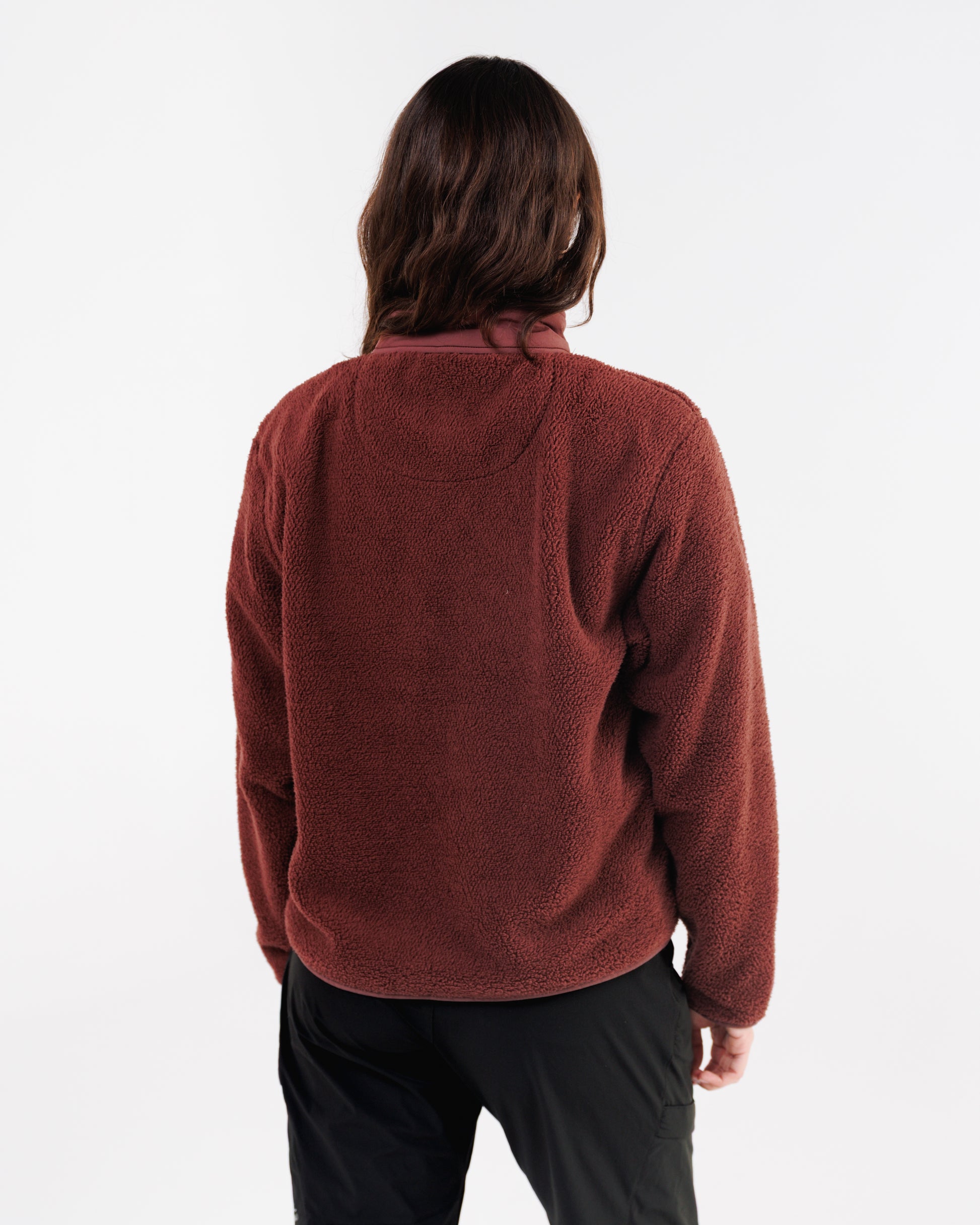 Back view of a woman wearing a maroon sherpa fleece jacket with black pants.