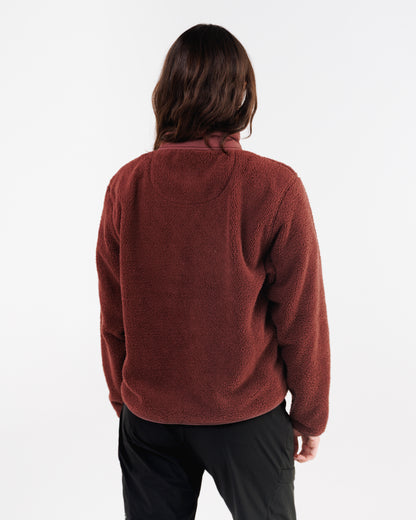 Back view of a woman wearing a maroon sherpa fleece jacket with black pants.
