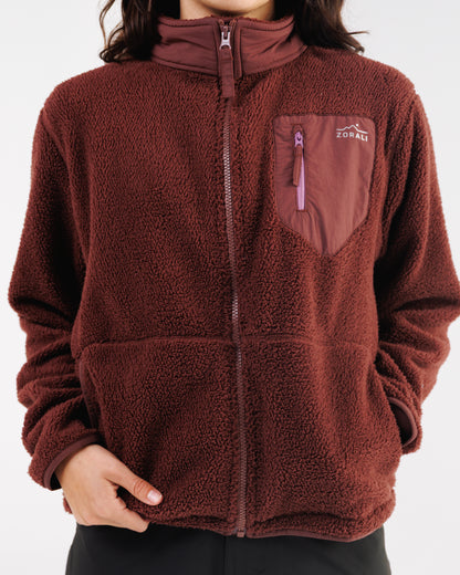 Woman wearing a maroon sherpa fleece jacket, close-up front view with hand at the chest pocket zipper.