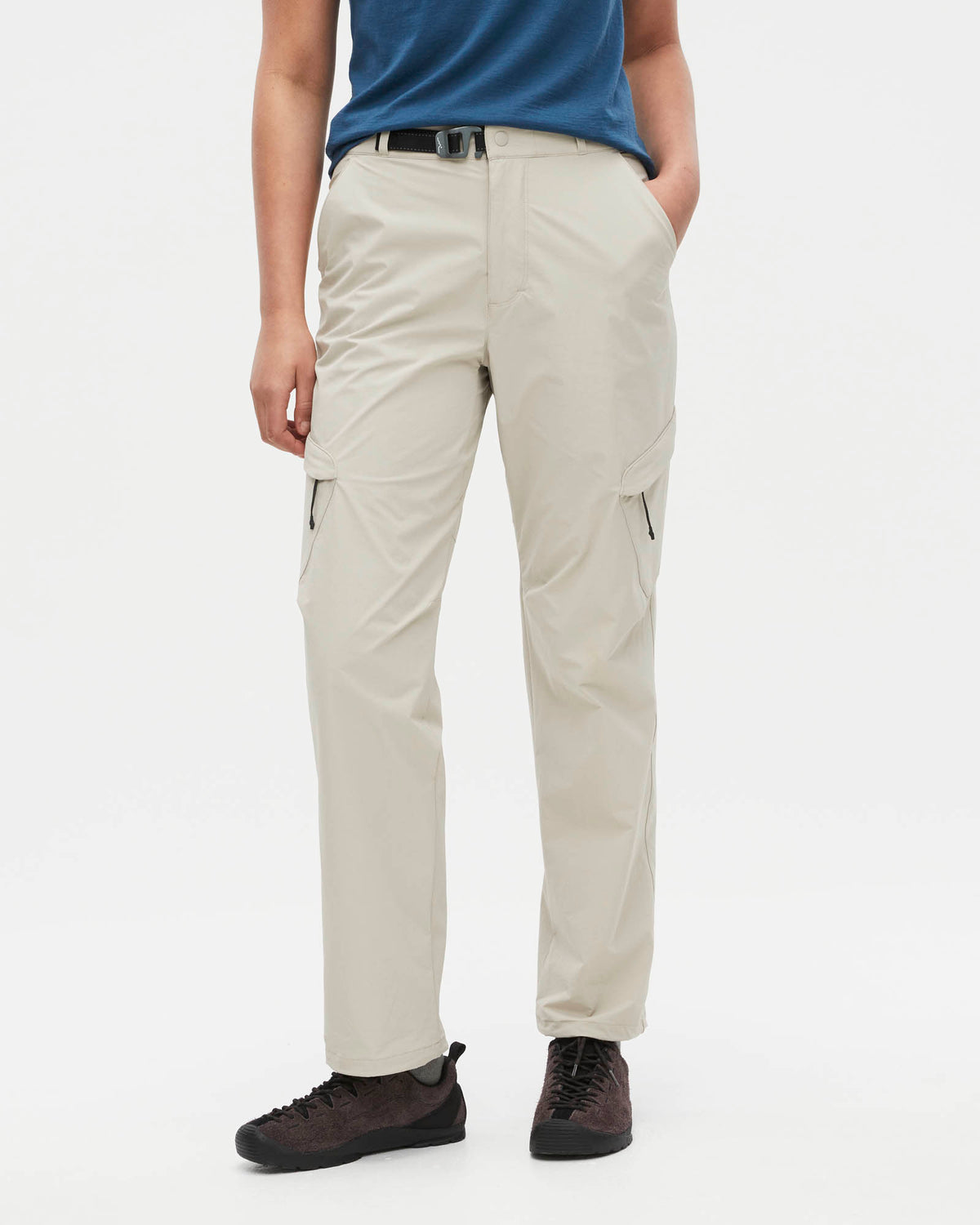 A person wearing light beige cargo pants with a blue shirt and dark brown shoes, shown from the waist down against a plain white studio background.