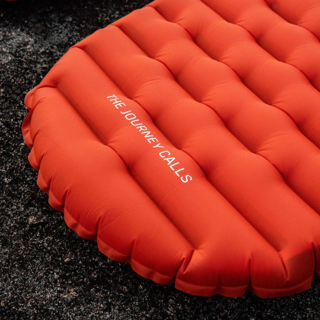 Orange inflatable camping mattress with 'The Journey Calls' text on a dark surface