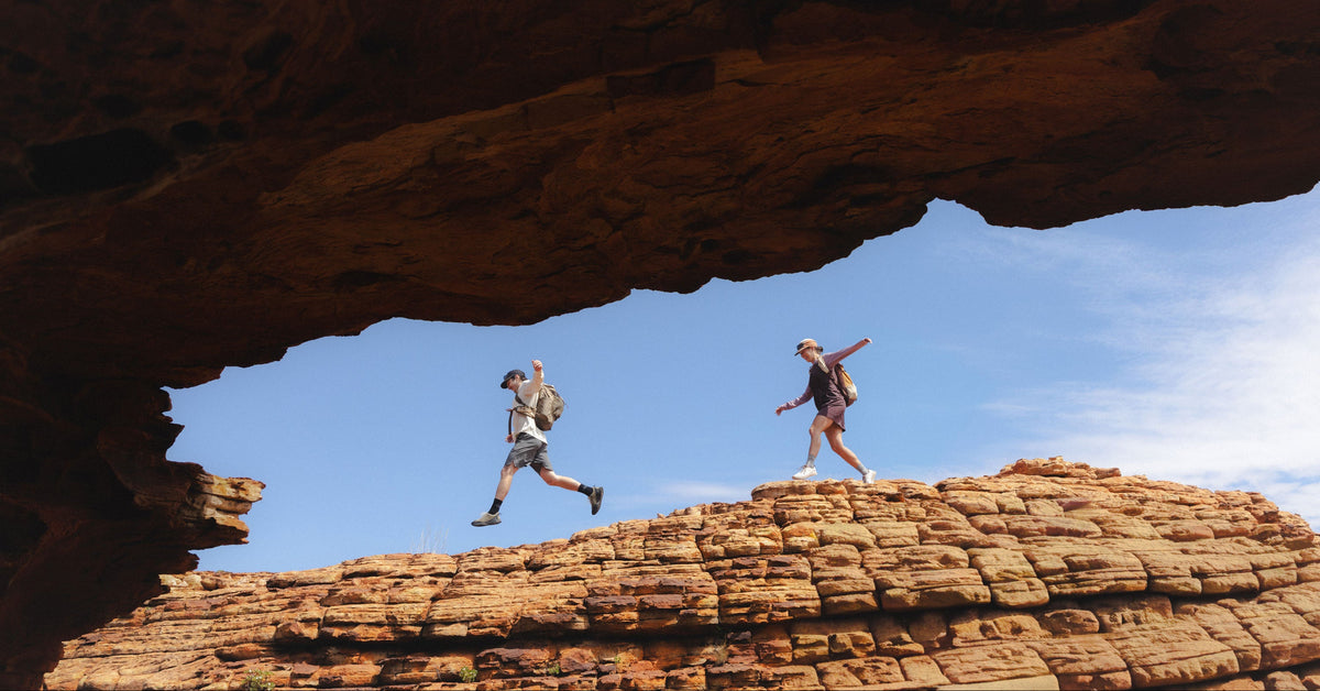 Two hikers walking a sandstone ridge under a rock arch in the Daylight collection