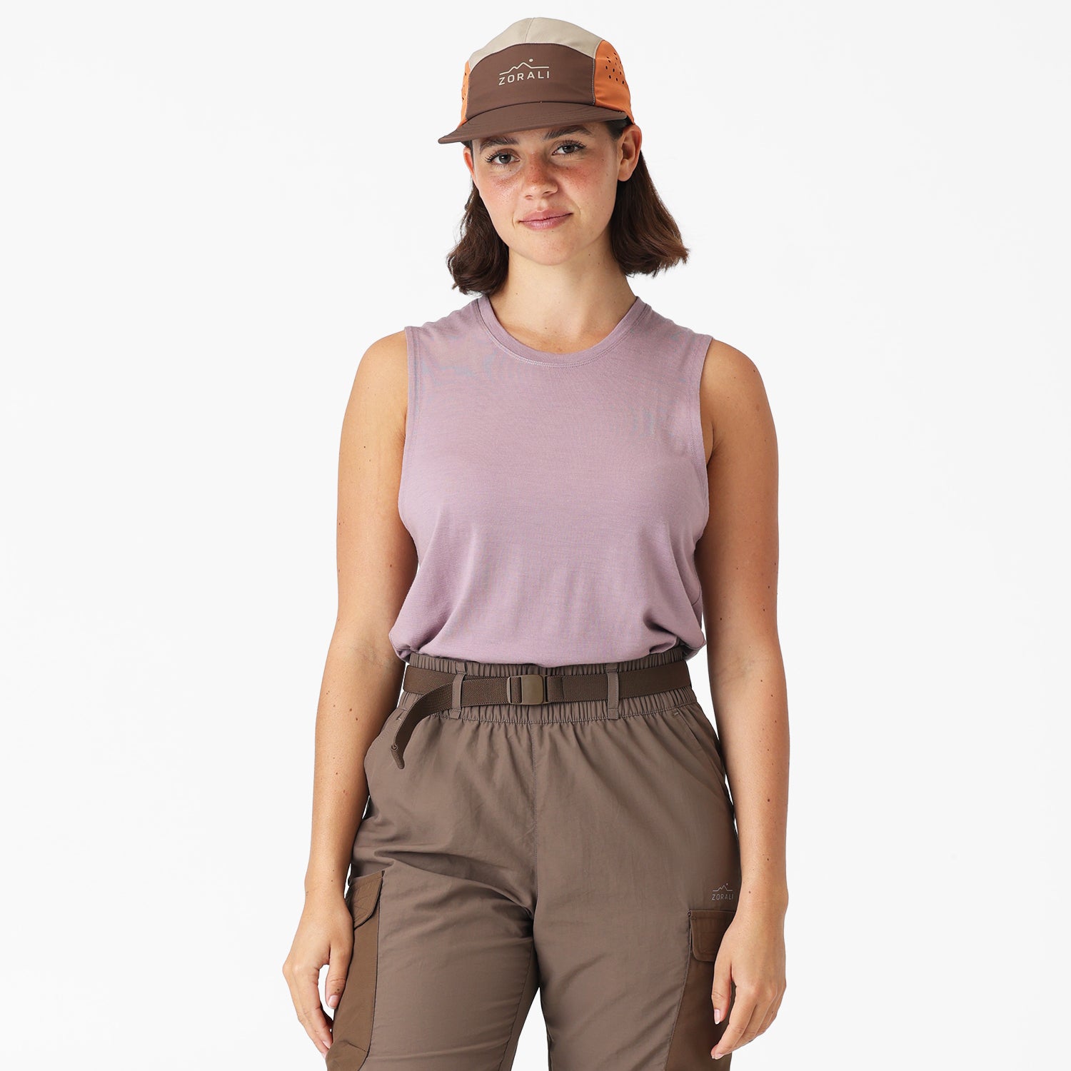 Woman wearing a sleeveless purple top and brown pants with a cap on a white background