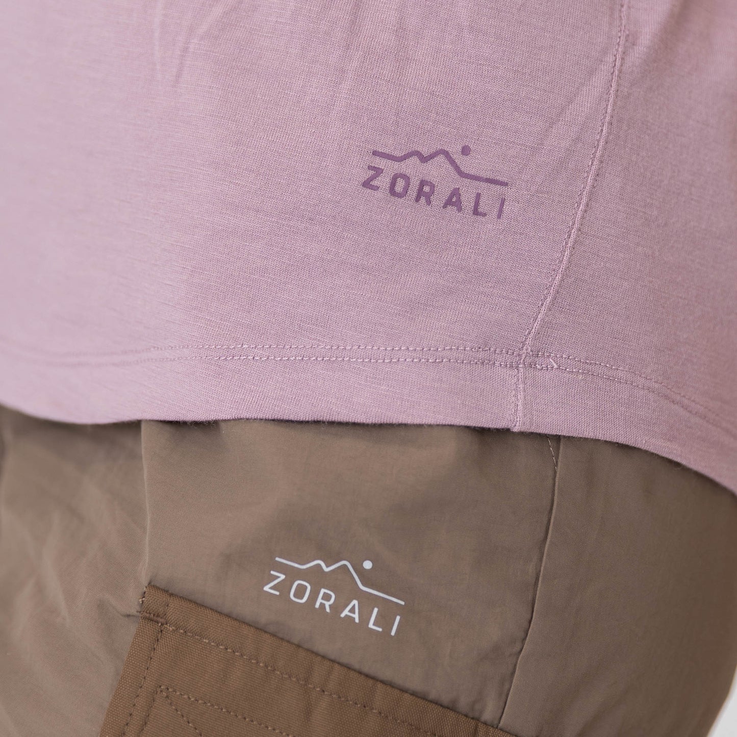 Close-up of a pink shirt and brown pants with ZORALI logo on clothing.