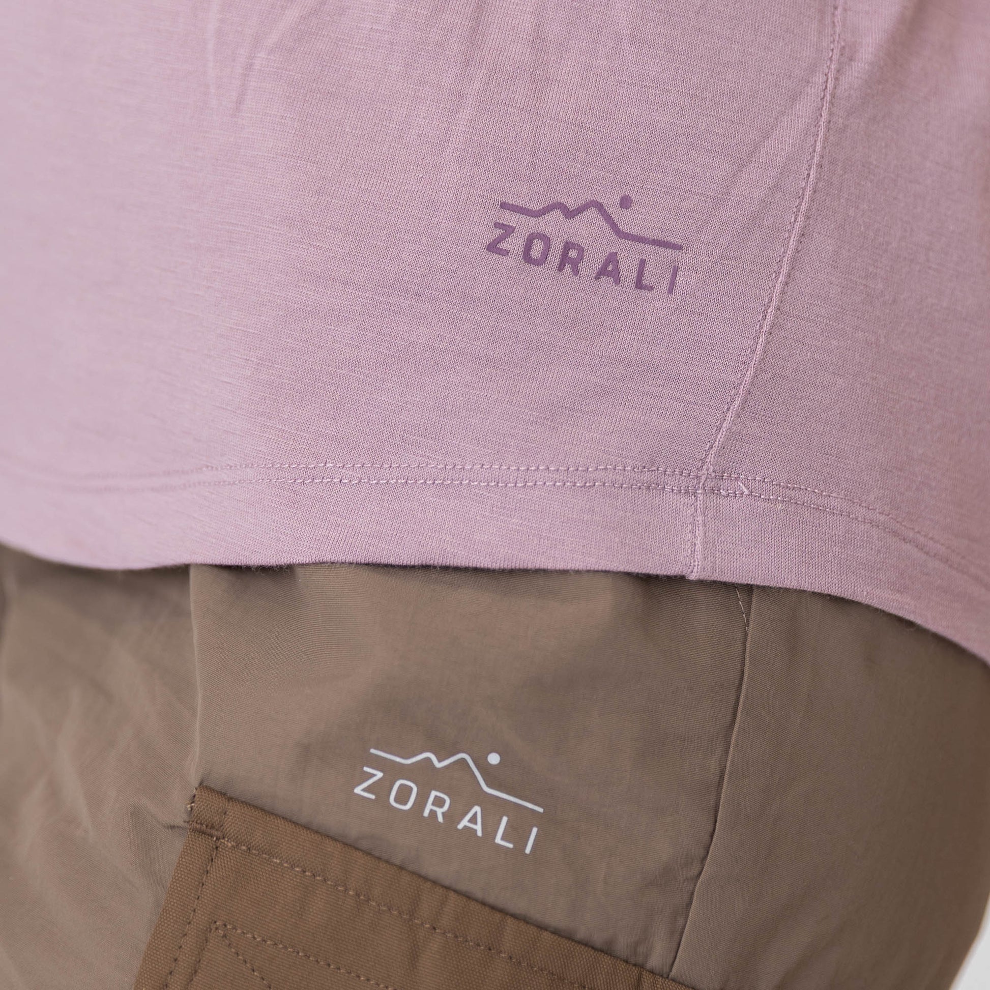 Close-up of a pink shirt and brown pants with ZORALI logo on clothing.
