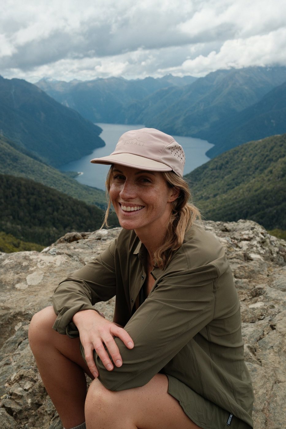Smiling on a summit rock above the lake in the Air-Trek Cap, Pink Sand