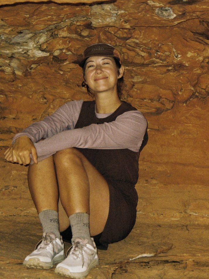 Hiker sitting in a sandstone cave in the Daylight™ Motion Dress in Cacao