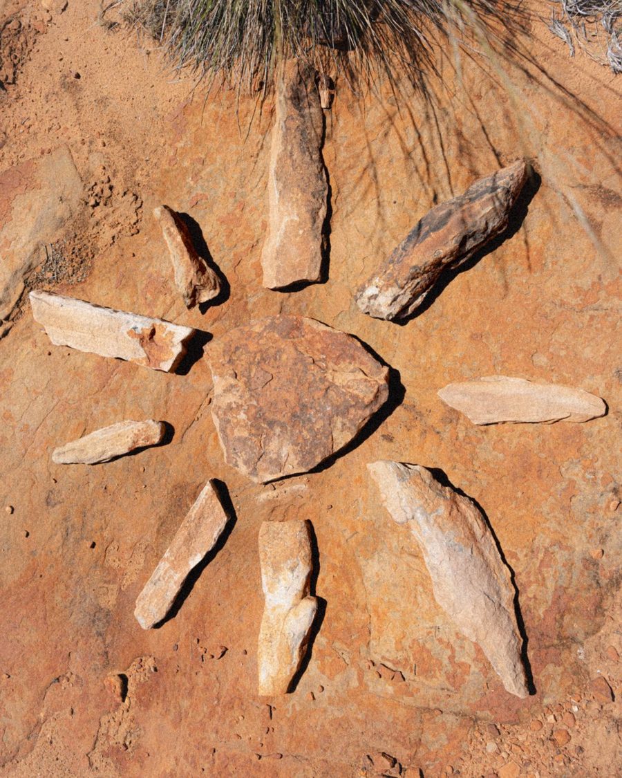 A sun drawn in red sand with stones